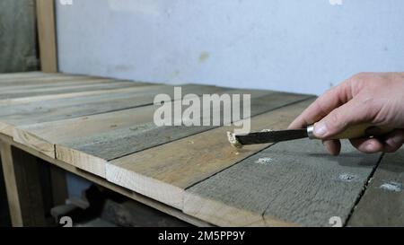 riempire fori e crepe su una superficie di legno con una cazzuola stretta in mano di un uomo, rattoppando irregolarità su una struttura fatta di tavole grezze Foto Stock