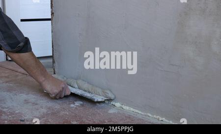 intonacare una parete della stanza con una malta elastica utilizzando una spatola larga, livellando la superficie della parete con stucco applicato su una cazzuola larga, lavori di finitura Foto Stock