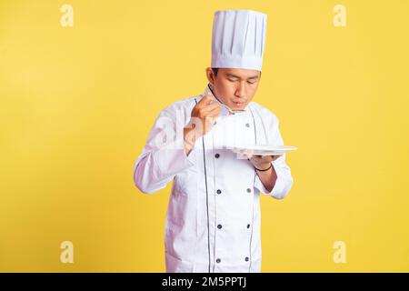 lo chef maschile assaggia il cibo mentre tiene il piatto di servizio vuoto Foto Stock