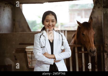 sorridente veterinario asiatico femmina in piedi con stalla cavallo Foto Stock