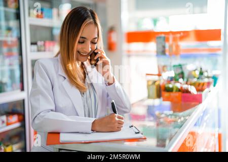 la farmacista femminile riceve la chiamata dal cliente e scrive la richiesta Foto Stock