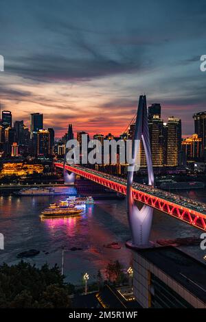 Una vista verticale del Ponte Qiansimen sul fiume di notte, con un incrociatore che passa sotto, e Chongqing World Financial Centre sullo sfondo Foto Stock