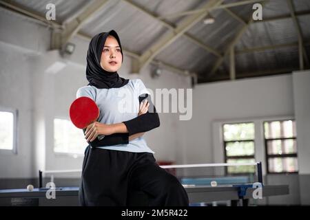 atleta femminile in hijab tenendo pipistrello con mani incrociate Foto Stock