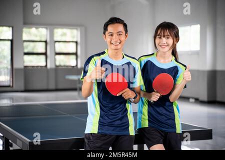 Due atleti asiatici sorridenti che tengono pagaia con i pollici in su Foto Stock
