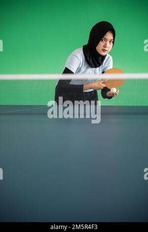 Atleta asiatico femminile in hijab servire mentre si gioca a ping pong Foto Stock