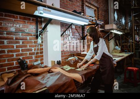 Giovane artigiano asiatico che lavora alla scrivania in tessuto di pelle Foto Stock
