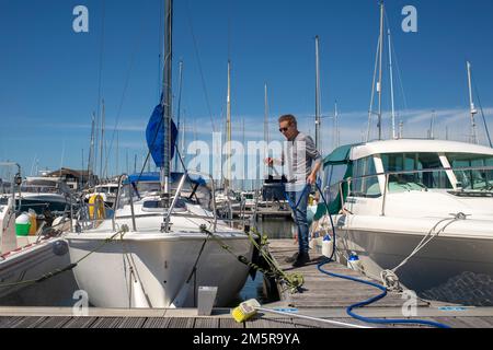 Uomo che lava e pulisce il suo yacht a vela in un porto turistico, manutenzione di barche, Foto Stock
