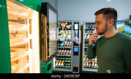 L'uomo caucasico acquista succo d'arancia appena spremuto dal distributore automatico. Foto Stock