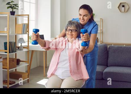 Donna anziana sorridente che solleva manubri, terapista che la assiste Foto Stock