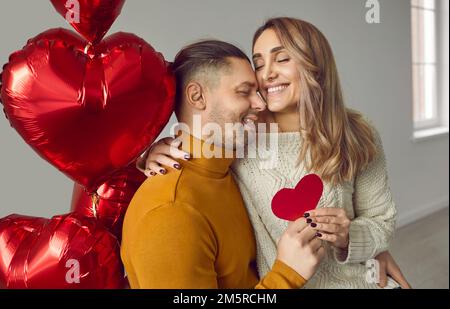 Giovane coppia innamorata in un'atmosfera romantica è seduta tra palloncini a forma di cuore nel soggiorno della casa. Foto Stock