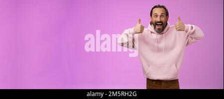 Eccitata energica, carismatica europea matura in rosa hoodie mostra pollici verso l'alto gesto sorridendo accordo di approvazione raccomandando Foto Stock