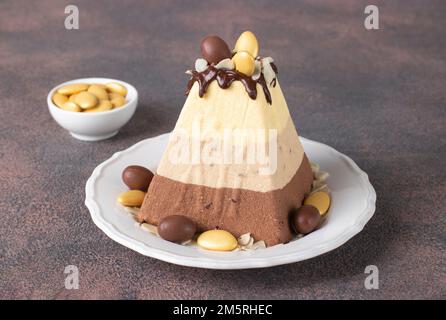 Tradizionale dessert di formaggio di Pasqua casetta fatto di tre tipi di cioccolato - bianco, latte e nero, decorato con uova di cioccolato su tavolo marrone Foto Stock