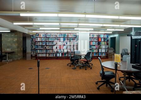 Libri su scaffali con sedie vuote e tavoli in biblioteca illuminata presso l'UCLA Foto Stock