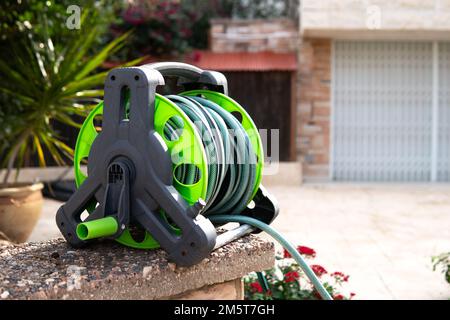 Bobina con un tubo da giardino avvolto nel cortile della casa Foto Stock