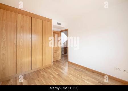 Una stanza vuota con una parete coperta da armadi a muro a quattro sezioni con porte in rovere e pavimenti in parquet di rovere francese Foto Stock