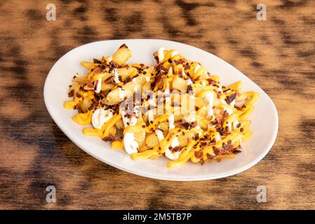 Un vassoio di porcellana bianco con un grande servizio di patatine fritte condite con vari tipi di formaggio fuso con pezzetti di pancetta fritta leggermente bruciata Foto Stock