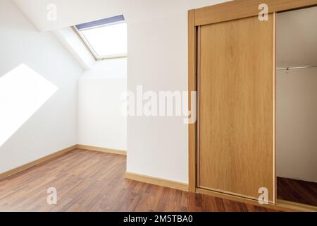 Camera al piano attico con soffitti mansardati, lucernari con persiane e armadio a muro con porte scorrevoli in legno e specchio Foto Stock