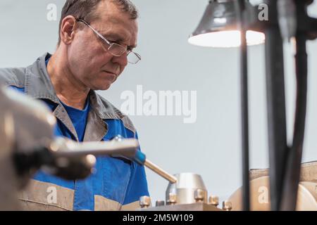 Ritratto di Turner con occhiali 50-55 anni al lavoro. La vecchia torretta metallica lavora in officina sulla macchina dietro il lavoro. Foto Stock