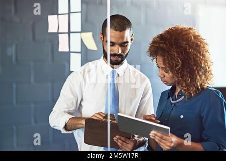Confronto di idee con un collega. due giovani professionisti del brainstorming con note appiccicose su una parete di vetro in un ufficio. Foto Stock