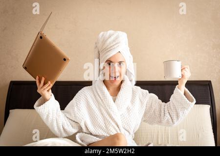 donna sorpresa in un vestito bianco. in una mano tiene un computer portatile nell'altra una tazza Foto Stock