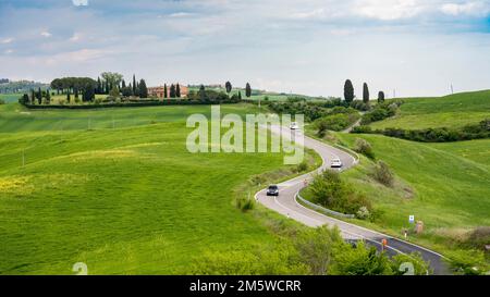 Agriturismo nel paesaggio collinare delle Crete Senesi con strada di campagna e auto, vicino ad Asciano, Toscana, Italia Foto Stock
