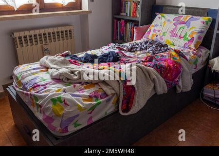 Il letto era disordinato in una camera. Coperta colorata, cuscini, lenzuola ondulate. Stile di vita, casa, routine mattutina. Foto Stock
