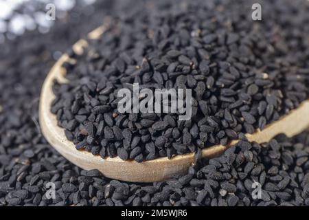 Primo piano di semi di Nigella neri su un cucchiaio di metallo. Consistenza degli ingredienti su sfondo bianco. Foto Stock