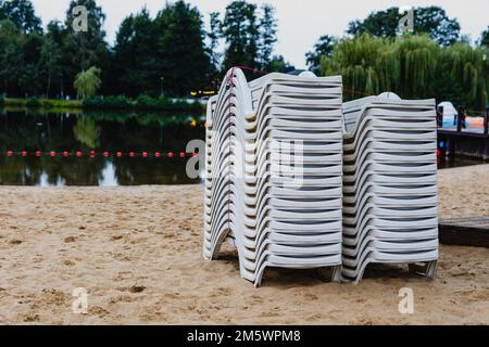 Dopo la stagione estiva, i lettini sulla spiaggia della città si stackano accanto allo stagno. La fine dell'attività ricreativa all'inizio dell'autunno Foto Stock