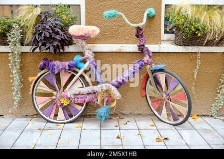Vecchia bicicletta colorata vintage con decorazione a maglia in piedi sulla strada Foto Stock
