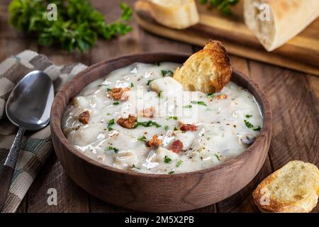 Zuppa di vongole del New england con pancetta, prezzemolo e pane francese tostato in un recipiente di legno Foto Stock