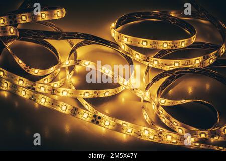 Dalla parte superiore di una striscia di luce LED non aggrovigliata con diodi luminosi su una superficie lucida al buio Foto Stock