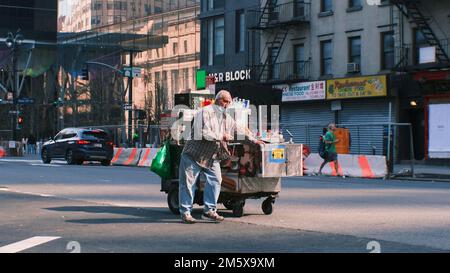 L'uomo di New York City spinge il suo carro dall'altra parte della strada Foto Stock