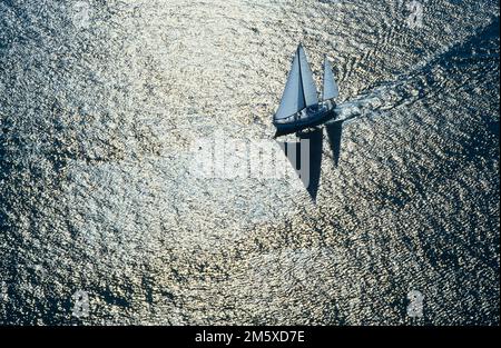 Vista Ariel verso il basso di una grande barca a vela sull'acqua con il sole del tardo pomeriggio che si riflette sull'acqua Foto Stock