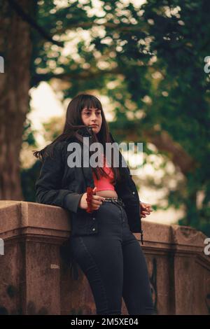 Una verticale di una bella giovane donna con scoppi che si posano per una foto mentre si appoggiano su un edificio in pietra Foto Stock