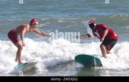 Cocoa Beach, Florida, USA - 24th dicembre 2021: Due surfisti tentano di fare un pugno all'evento annuale della vigilia di Natale di Cocoa Beach chiamato "Surfing Santas" Foto Stock