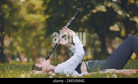 Una ragazza suona il clarinetto mentre sdraiata sull'erba nel parco. Foto Stock