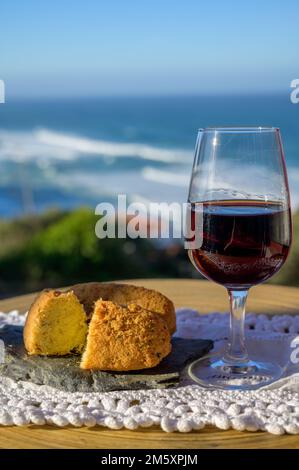 Abbinamento di cibo e bevande portoghesi, bicchiere di vino porto bruno e coccodrillo pastais de bacalhau, servito all'aperto con vista sul blu soleggiato Atla Foto Stock