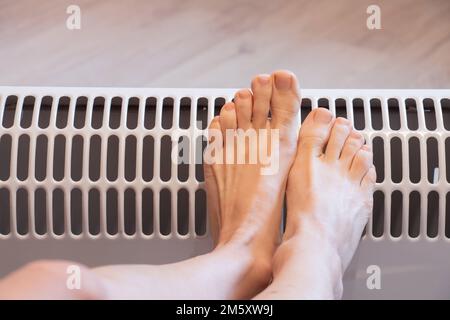 gambe femminili su una batteria a casa, stagione di riscaldamento, gambe calde su una batteria elettrica, gambe Foto Stock