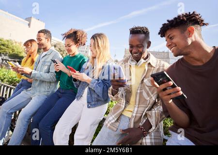 Gruppo di giovani di razza mista con telefoni cellulari. Studenti entusiasti che utilizzano dispositivi tecnologici Foto Stock