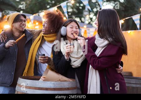 Amici felici che mangiano cioccolato con churros Street food in città la sera all'aperto Foto Stock