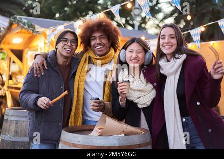 Amici felici che mangiano cioccolato con cibo di strada churros in città la sera all'aperto mangiando al cibo di strada stalla Foto Stock