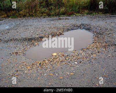 Pothole su una strada asfaltata in una giornata invernale piovosa. Concetto di rischio e problemi di traffico Foto Stock