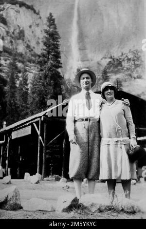 Una giovane coppia posa di fronte alle cascate Yosemite mentre in vacanza in California, ca. 1928. Foto Stock