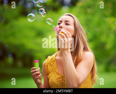 Perda i vostri problemi, soffia alcune bolle. una giovane donna spensierata che soffia bolle nel parco. Foto Stock