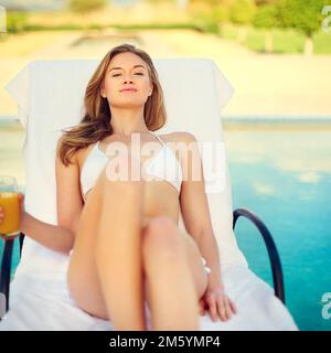 L'estate e il livin è facile. una giovane donna attraente che si gode un drink a bordo piscina. Foto Stock