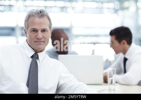 HES un grande capo. Ritratto di un uomo d'affari maturo seduto davanti a due colleghi più giovani. Foto Stock