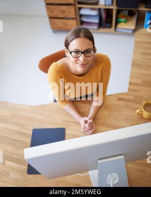 Puntando verso la parte superiore. Ritratto ad angolo alto di una giovane designer femminile alla sua scrivania. Foto Stock