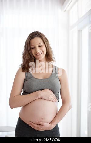 Disponibile a breve. una giovane donna incinta in piedi nella sua casa. Foto Stock