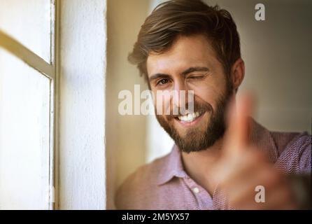 Fatelo con passione o con Per niente. Ritratto corto di un uomo d'affari che dà i pollici in su mentre levandosi in piedi dalla sua finestra dell'ufficio. Foto Stock