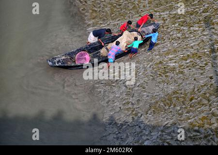 La famiglia dei pescatori ha visto sollevarsi la barca a terra più alta attraverso i fanghi fangosi delle mangrovie nell'area di Canning di Sundarbans. Canning si trova a quasi 100 km da Kolkata e nella zona sotto il delta di Sunderban sulle rive occidentali del fiume Matla. La maggior parte degli abitanti del delta sono pescatori che si trovano ad affrontare sfide in quanto l'oceano inghiottisce terra nella più grande foresta di mangrovie del mondo, esseri umani e tigri vengono schiacciati in uno spazio sempre più ridotto nei Sundarbans indiani, con conseguenze letali. Il livello del mare è aumentato in media di 3 - 5 centimetri all'anno negli ultimi due decenni Foto Stock